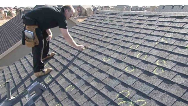 Professional on an asphalt roof inspecting the ridge of the structure